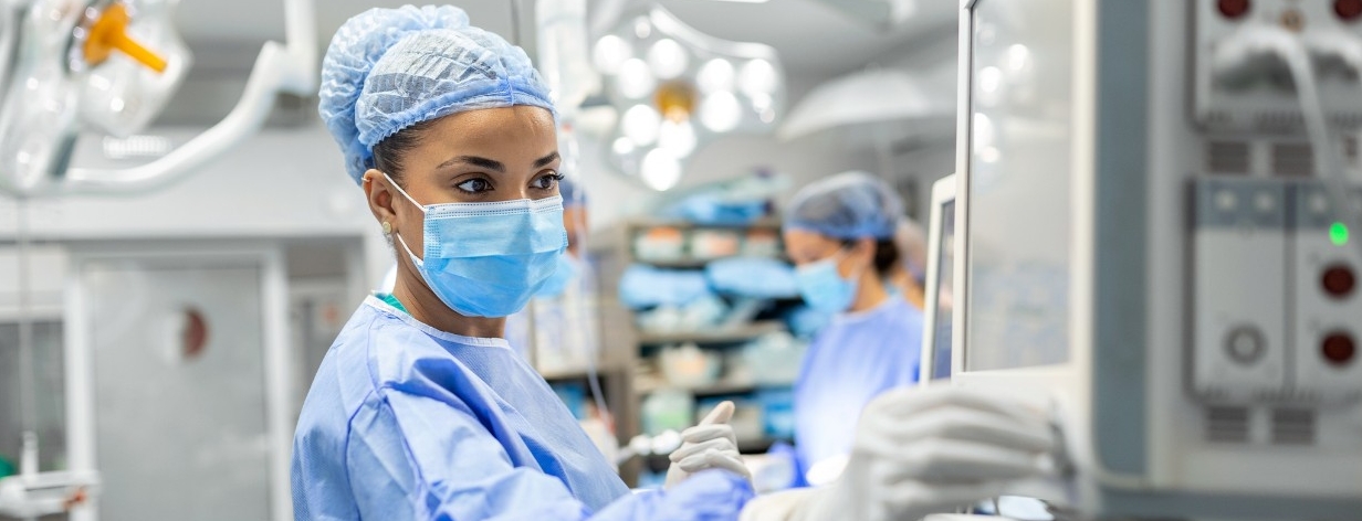 1410045037 Anesthetist Working In Operating Theatre Wearing Protecive Gear checking monitors while sedating patient before surgical procedure in hospital